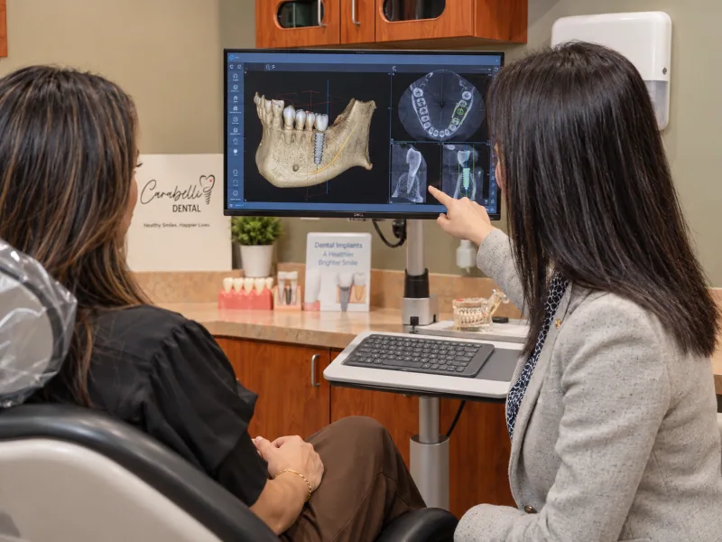 A dentist examining a three-dimensional jaw scan while explaining an implant treatment plan.
