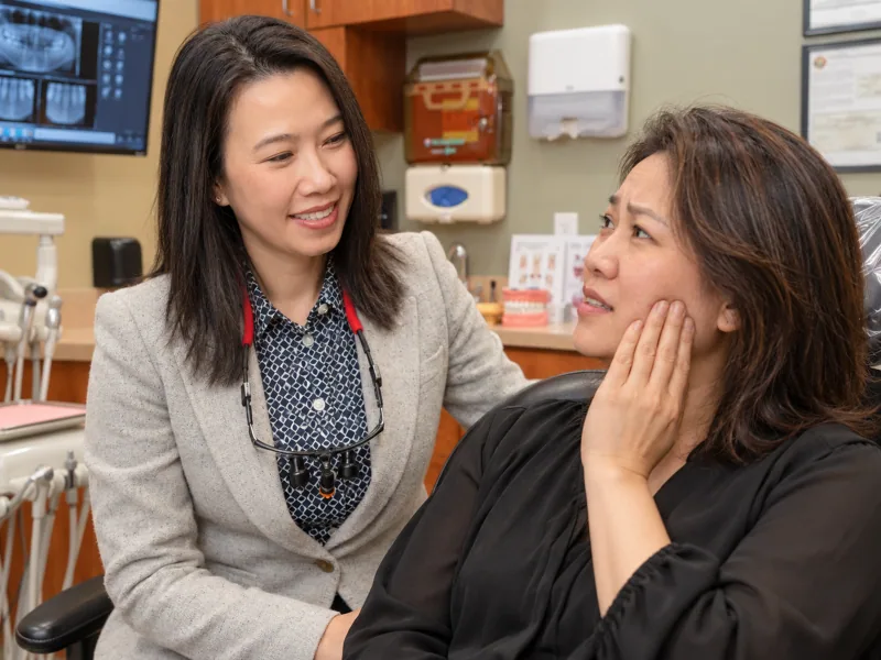 A dentist listening to an adult patient describe tooth discomfort before a focused examination.